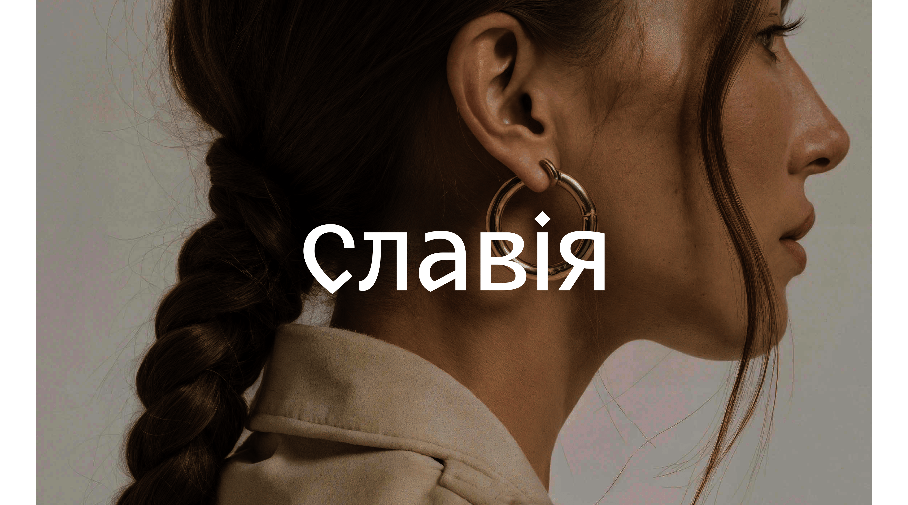 Женщина с косым хвостом и золотыми серьгами-обручами изображена в профиль на нейтральном фоне. Поперек изображения крупными белыми кириллическими буквами написано слово Славія (Славия), подчеркивающее бренд Славия.